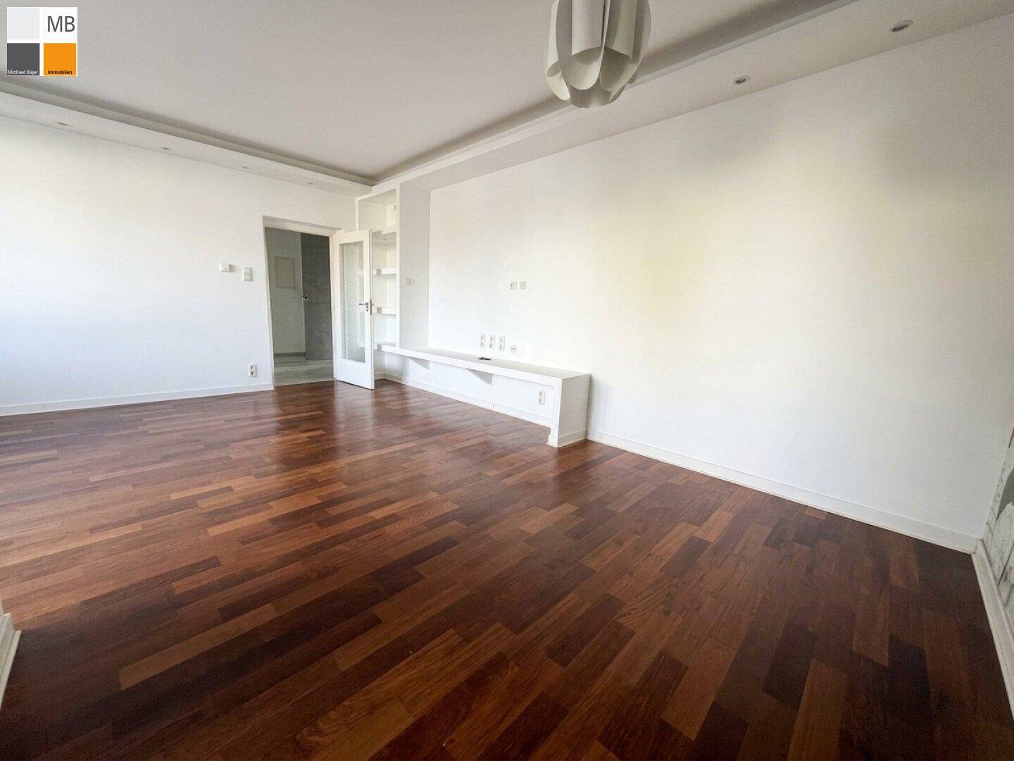 Geräumiges Wohnzimmer mit dunklem Parkettboden und weißer Wandgestaltung.