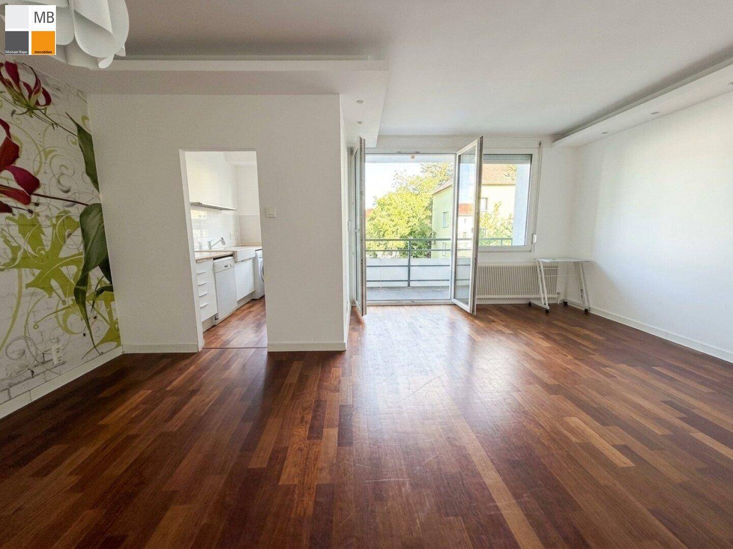 Wohnzimmer mit Parkettboden, floraler Tapete und Blick in die Küche.