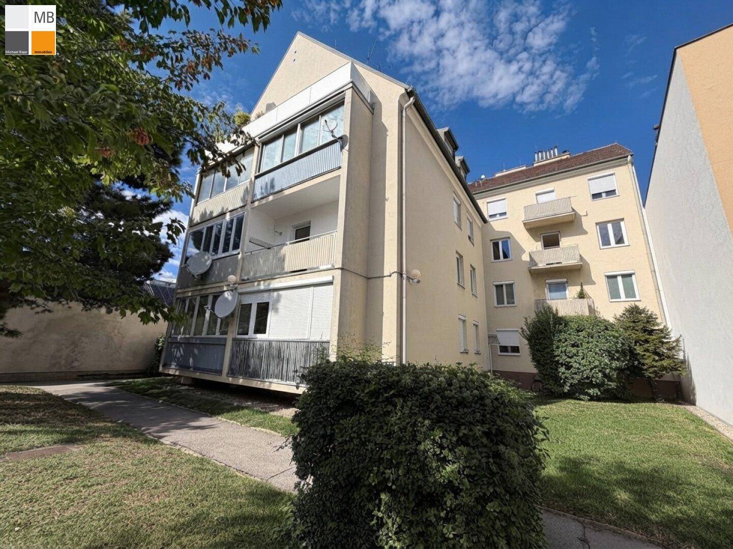 Außenansicht eines Mehrfamilienhauses mit Balkonen und gepflegten Grünflächen im Vordergrund.
