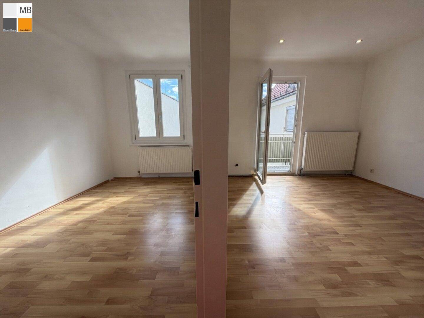 Heller, leerer Raum mit Laminatboden, weißen Wänden und Zugang zu einem Balkon.