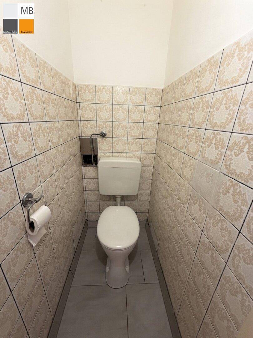 Separate Toilette mit gemusterten Fliesen an den Wänden und einem Steh-WC.