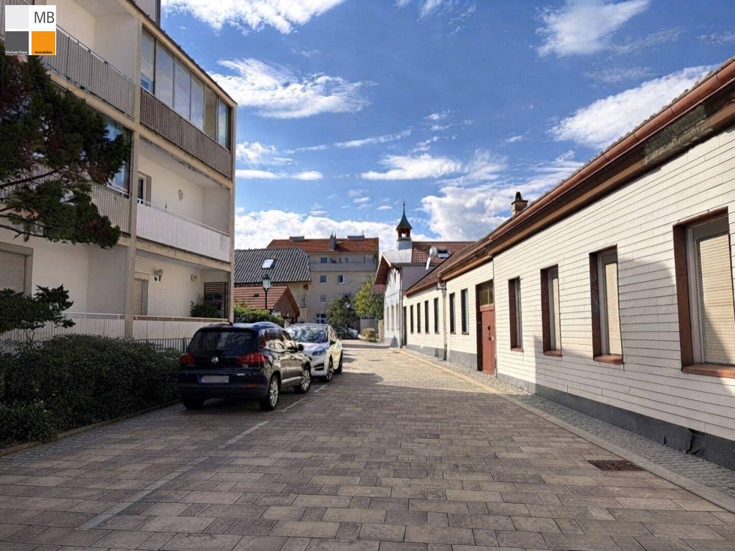 Ruhige Wohnstraße mit geparkten Autos und traditionellen Gebäuden unter blauem Himmel.