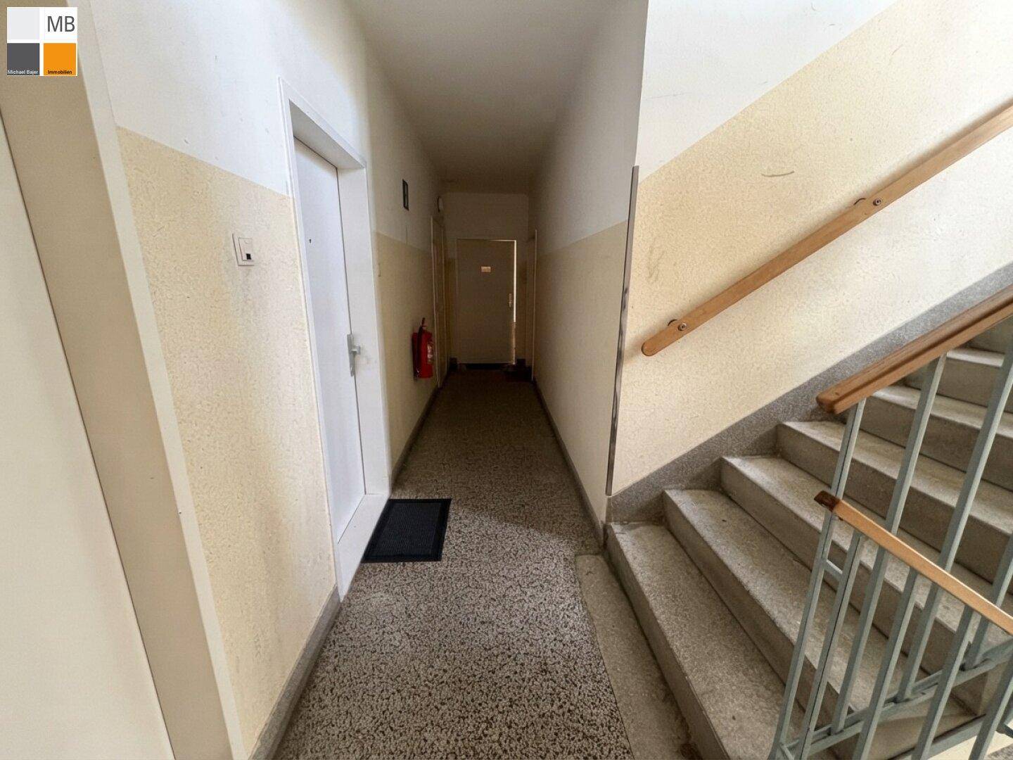 Treppenhaus und Flur eines Mehrfamilienhauses mit Terrazzoboden und Holzgeländer.