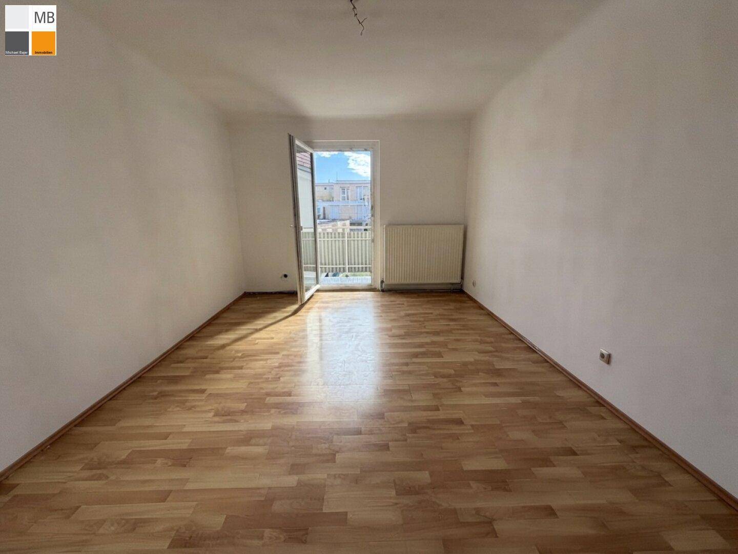 Geräumiger, heller Raum mit Laminatboden und offener Balkontür, die viel Licht hereinlässt.