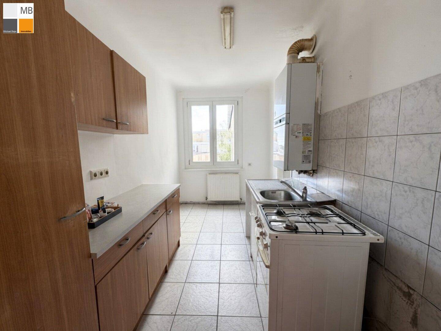 Einfache Küche mit Holzschränken, Gasherd und Fliesenboden, bereit zur Modernisierung.