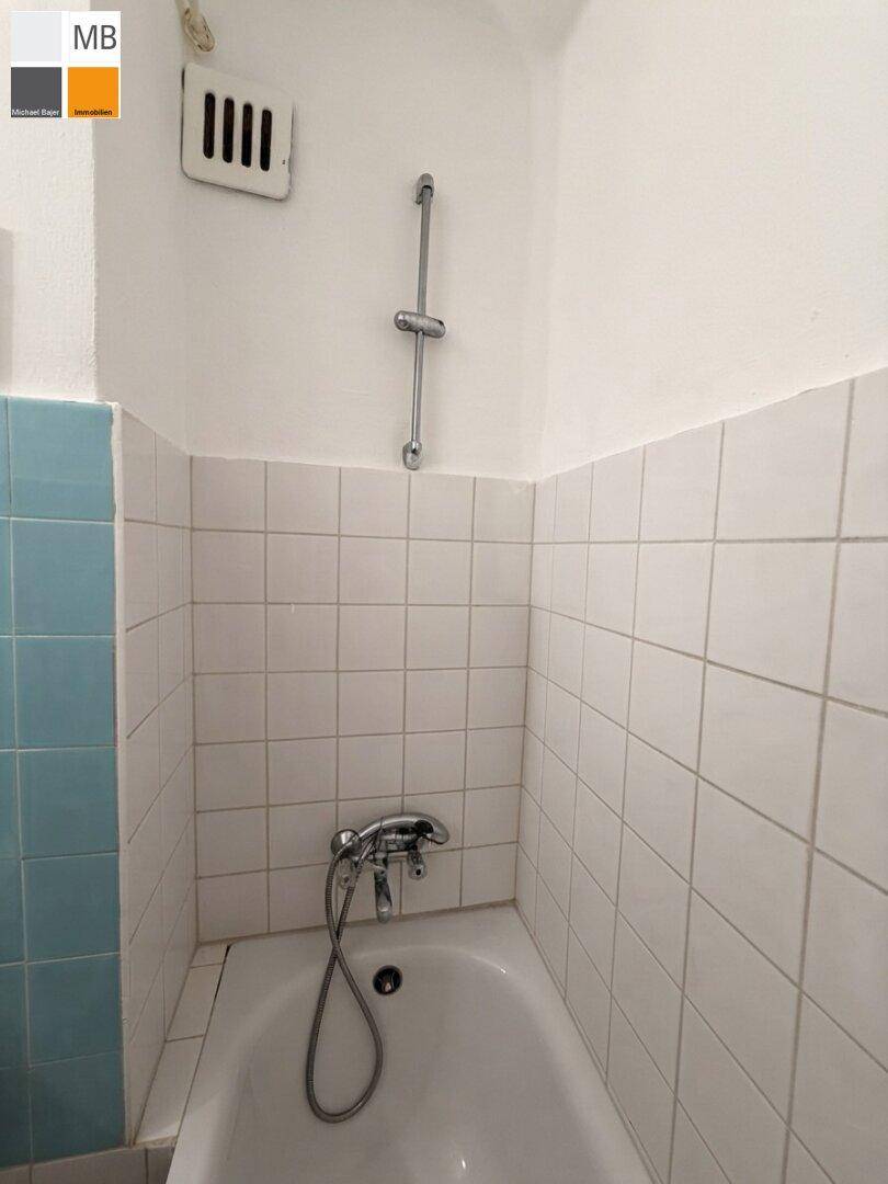 Badezimmer mit Badewanne, Duscharmatur und weißen Wandfliesen, funktional und einfach.
