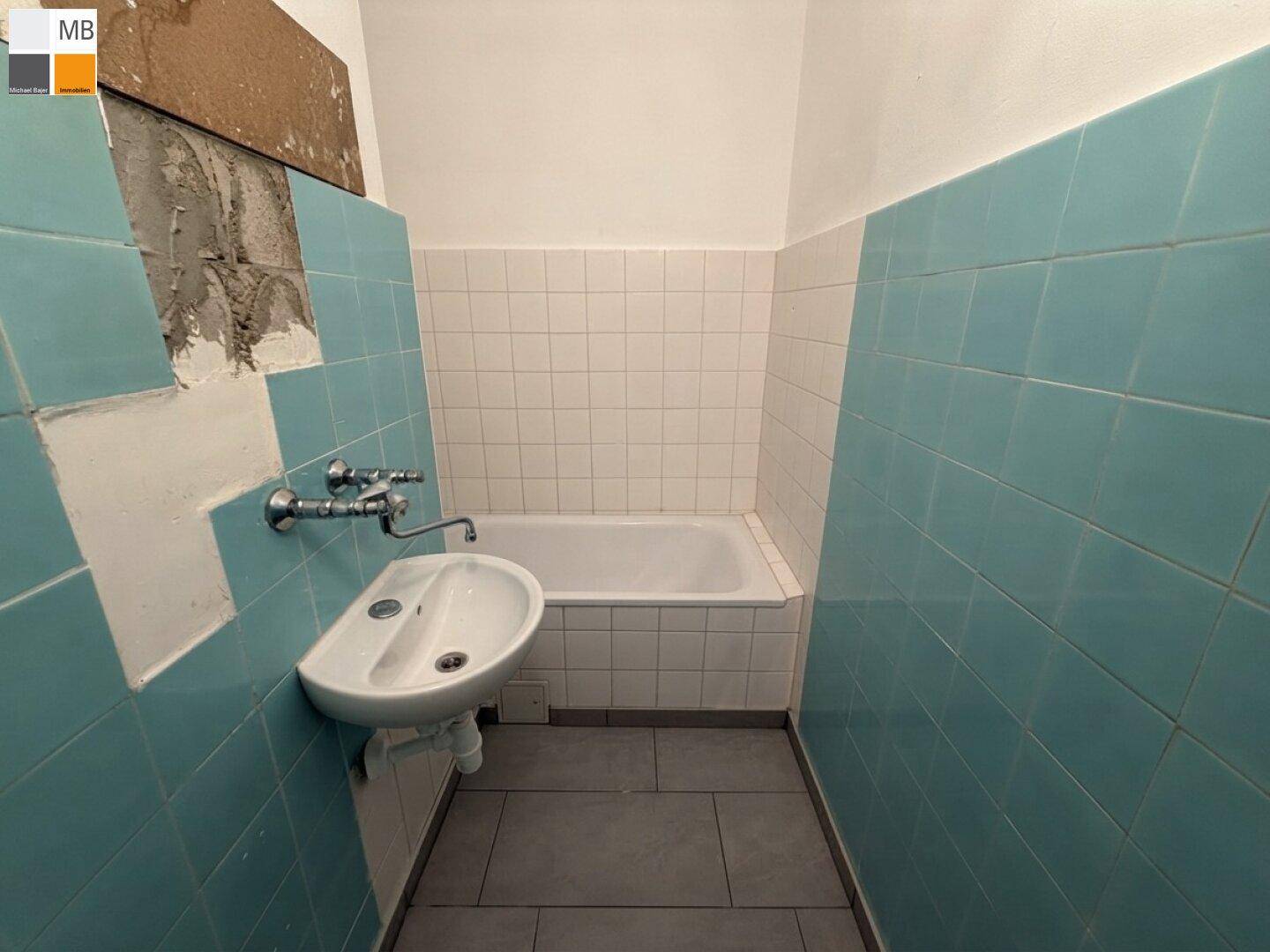 Badezimmer mit blauen und weißen Fliesen, Badewanne und einem kleinen Waschbecken.