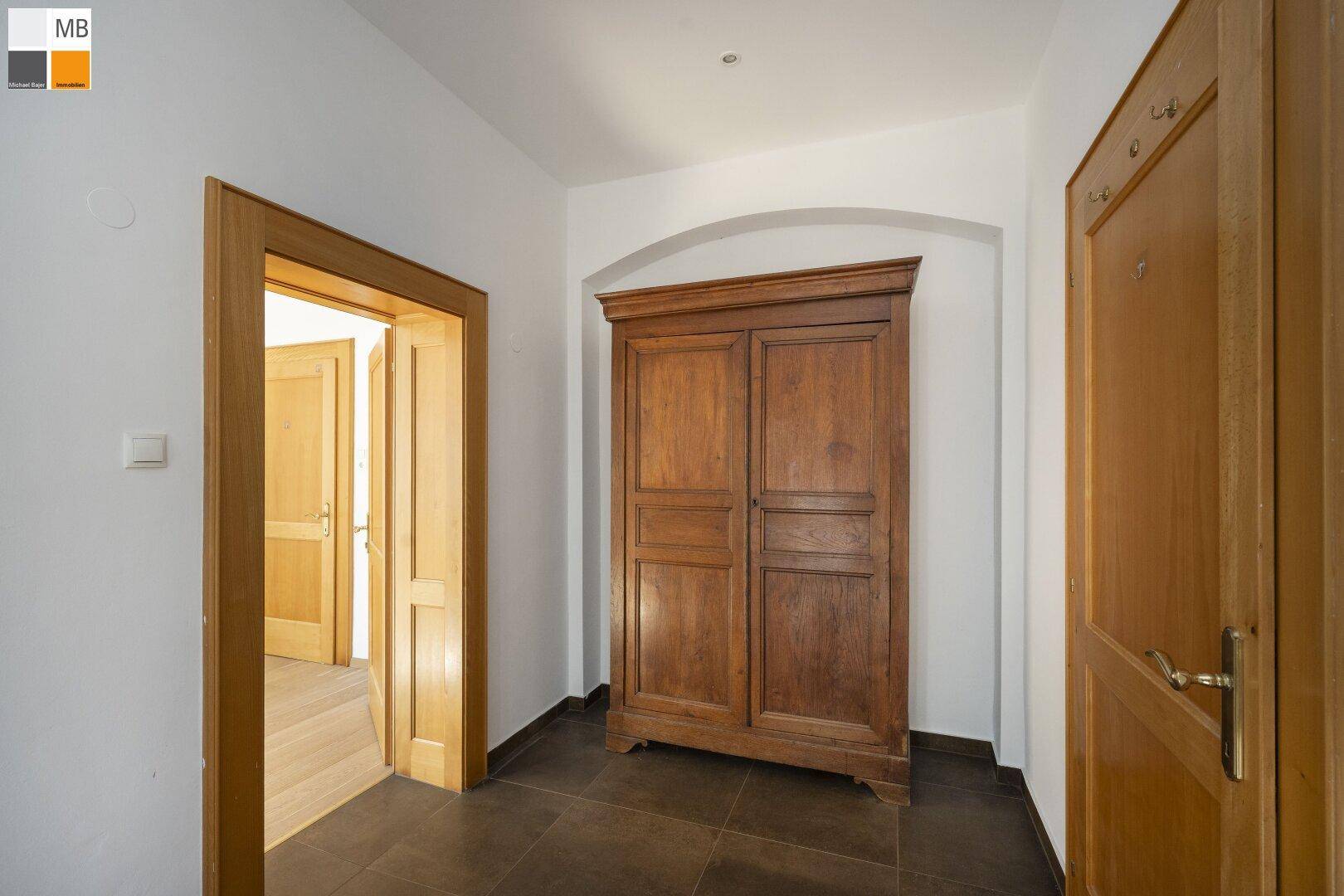 Geräumiger Flur mit dunklem Fliesenboden und einem antiken Holzschrank.