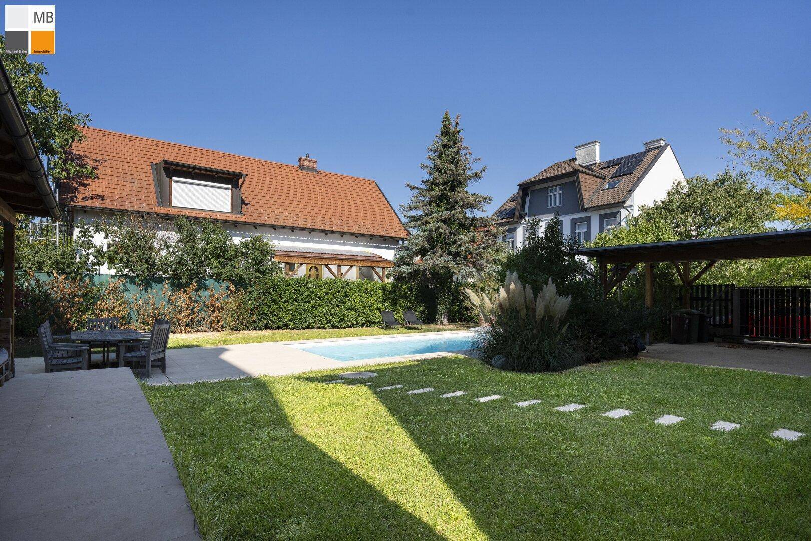 Gepflegter Garten mit Pool, Rasenfläche und überdachtem Carport im Hintergrund.