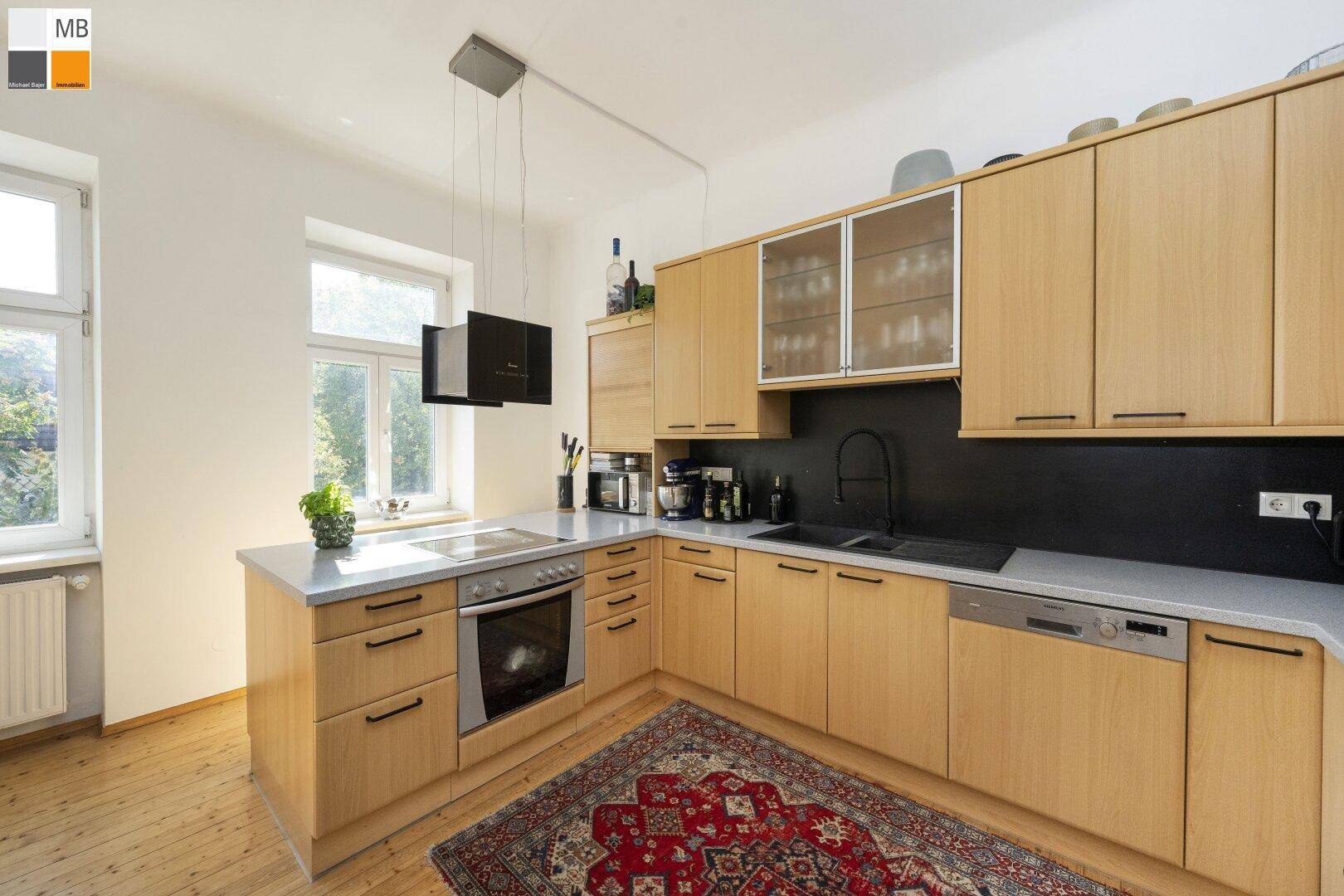 Helle Küche mit Holzschränken, integriertem Backofen und großem Fenster für Tageslicht.