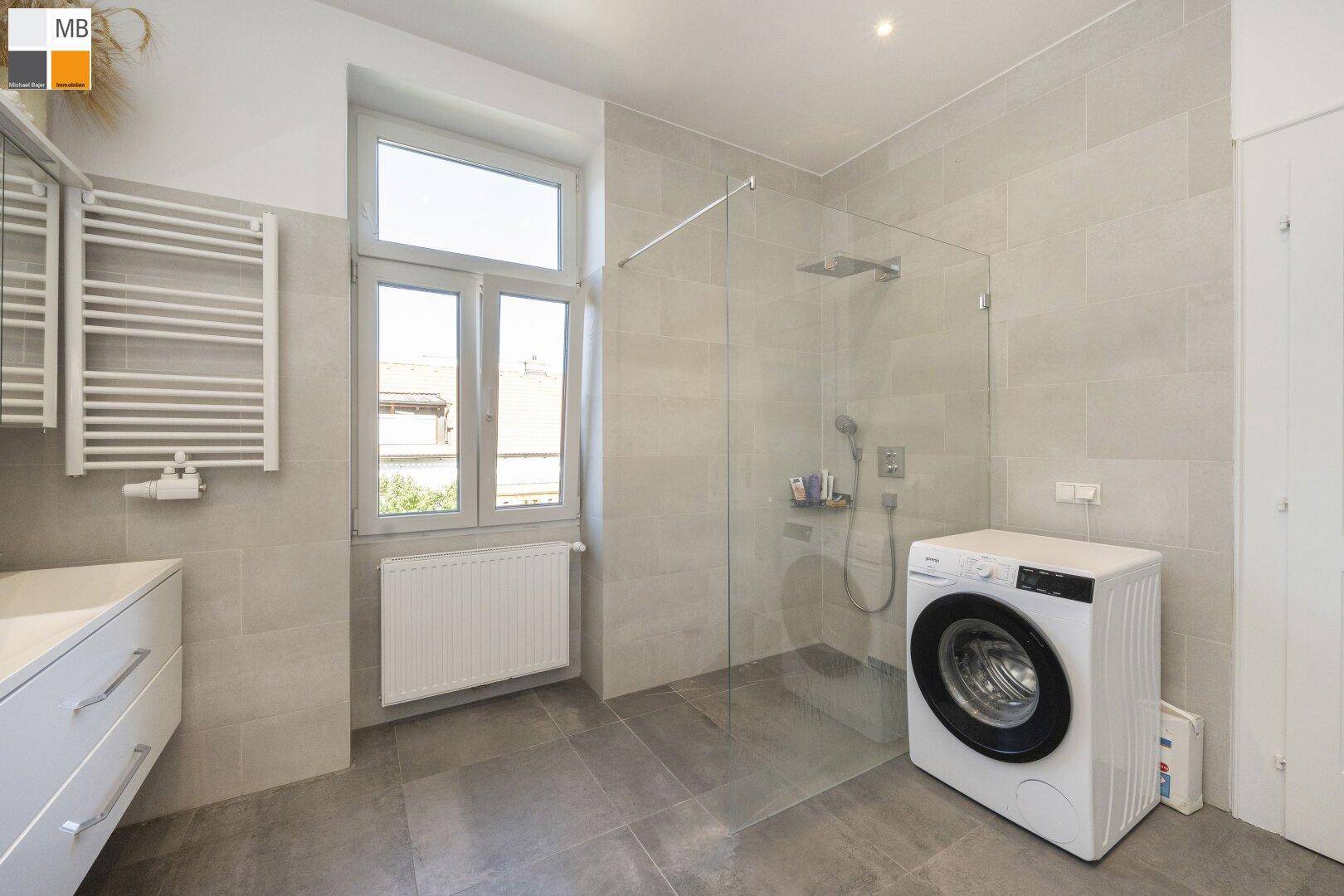 Geräumiges Badezimmer mit ebenerdiger Dusche, Waschmaschine und Fenster.