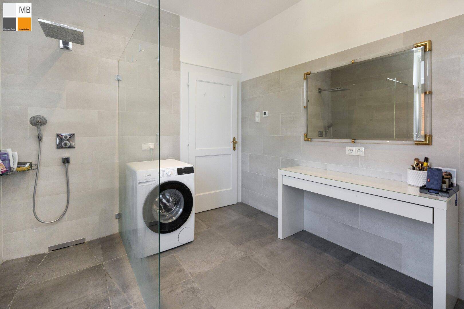 Helles Badezimmer mit großer Dusche, Waschmaschine und stilvollem Spiegel.