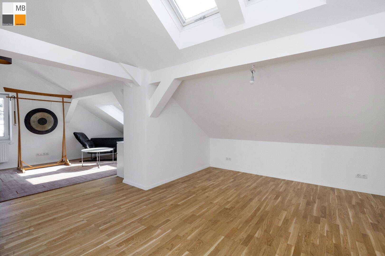 Offener Dachbodenraum mit Holzboden, sichtbaren Balken und viel Tageslicht.