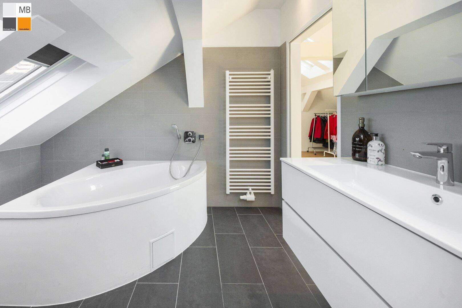 Modernes Badezimmer im Dachgeschoss mit Eckbadewanne, grauen Fliesen und Handtuchheizkörper.