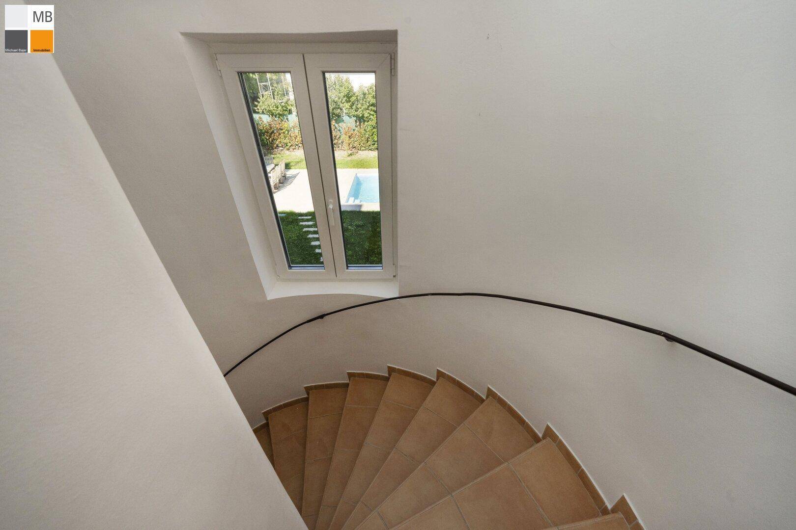 Wendeltreppe mit Terrakotta-Stufen und Blick auf den Garten durch das Fenster.