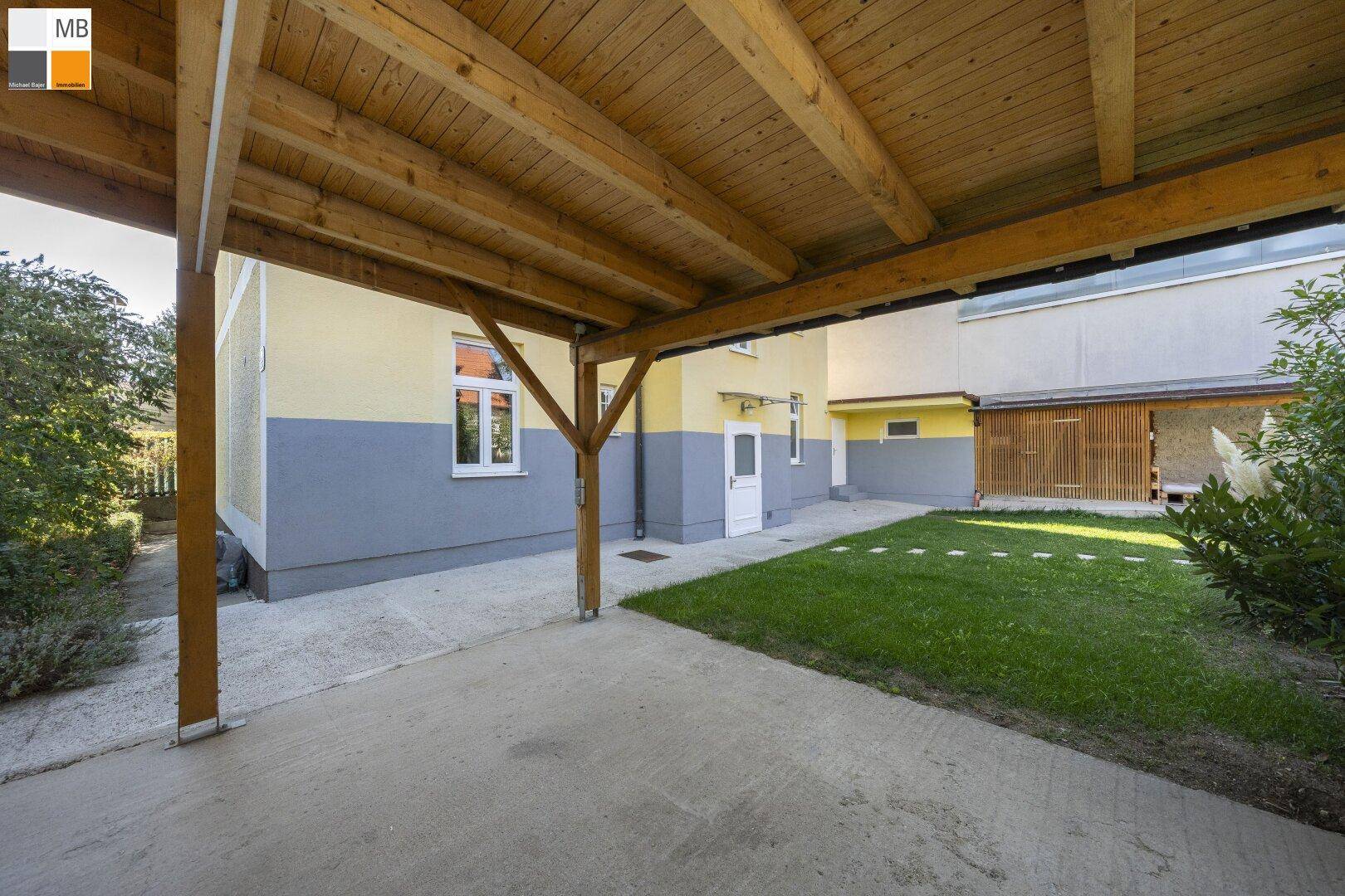 Überdachter Carport mit Holzbalken und angrenzender Grünfläche.