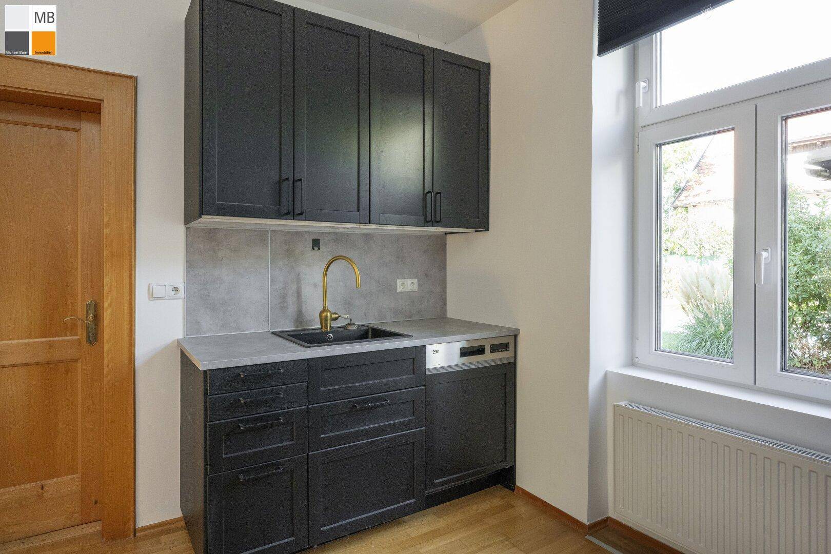 Funktionale Küche mit schwarzen Unterschränken, Spülmaschine und Fenster für natürliches Licht.