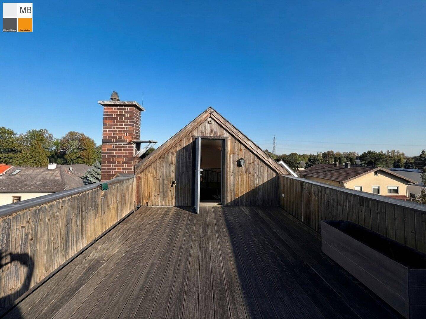 Weitläufige Dachterrasse mit Holzboden und Zugang zum Innenbereich, umgeben von grüner Landschaft.