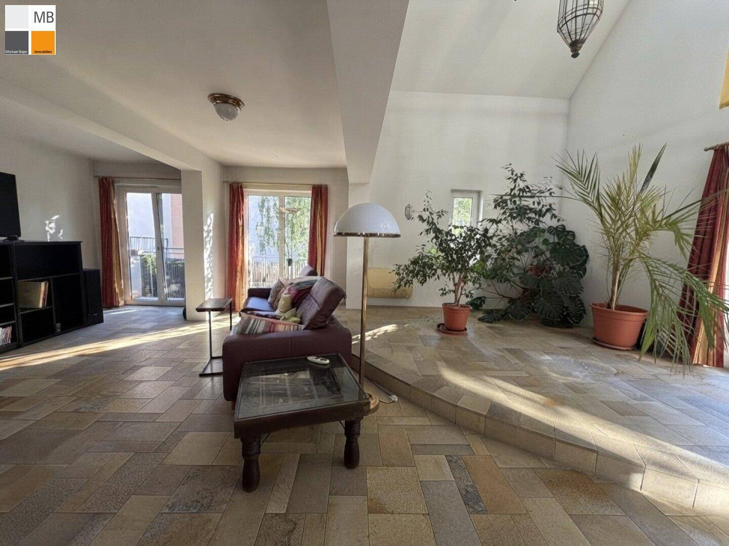 Helles Wohnzimmer mit beigefarbenen Fliesen, gemütlicher Sitzecke und großen Fenstern zum Garten.
