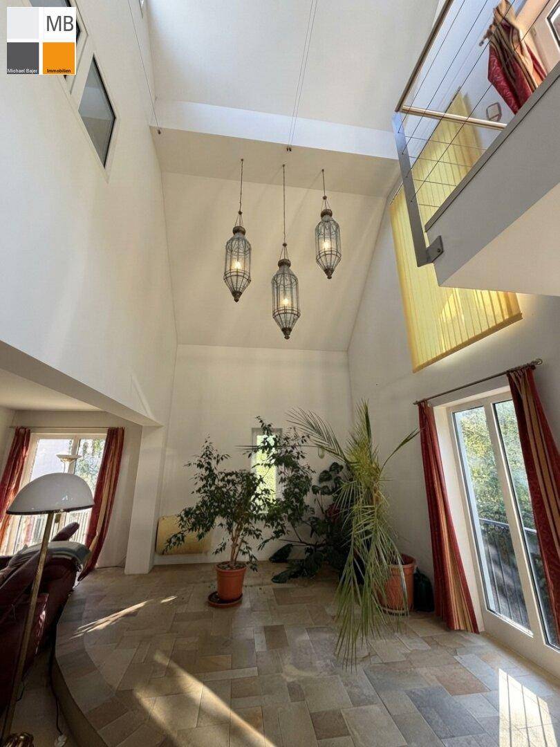Lichtdurchfluteter Wohnbereich mit sehr hohen Decken, dekorativen Hängelampen und einer Galerie.