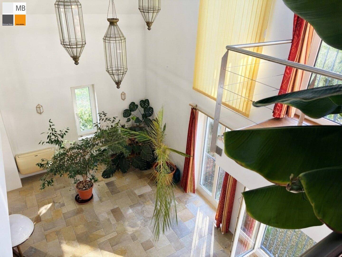 Blick von der Galerie in den lichtdurchfluteten Wohnbereich mit hohen Decken und vielen Pflanzen.