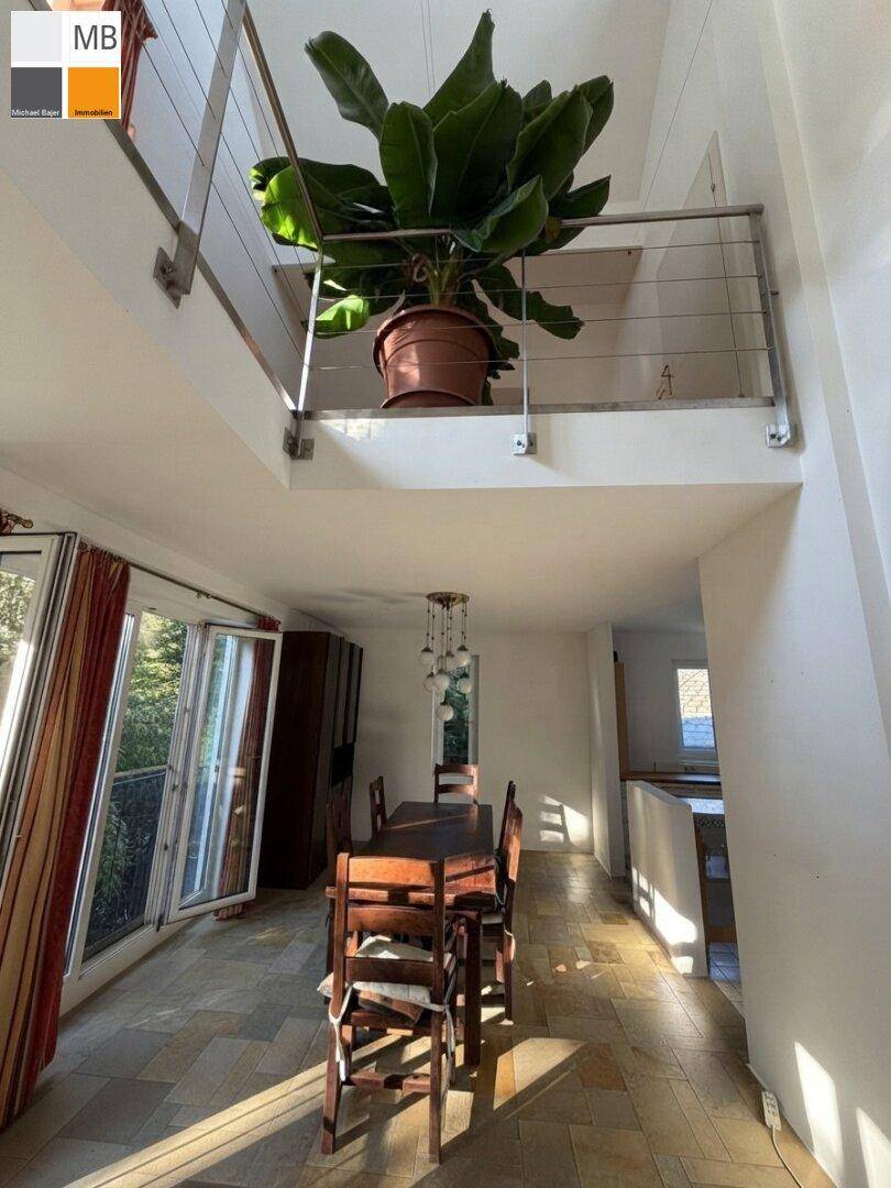 Heller Essbereich mit Holztisch und Blick auf die Galerie, umgeben von großen Fenstern.