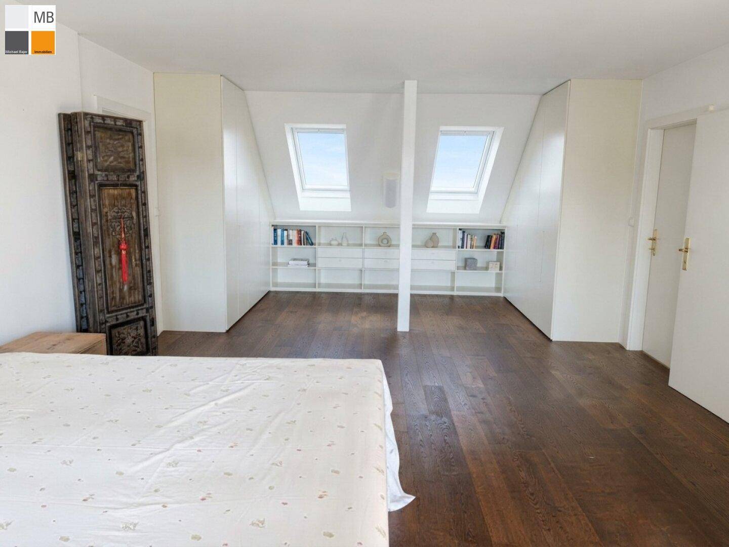 Geräumiges Schlafzimmer mit Holzboden, Dachschrägen und integrierten Regalen unter den Dachfenstern.