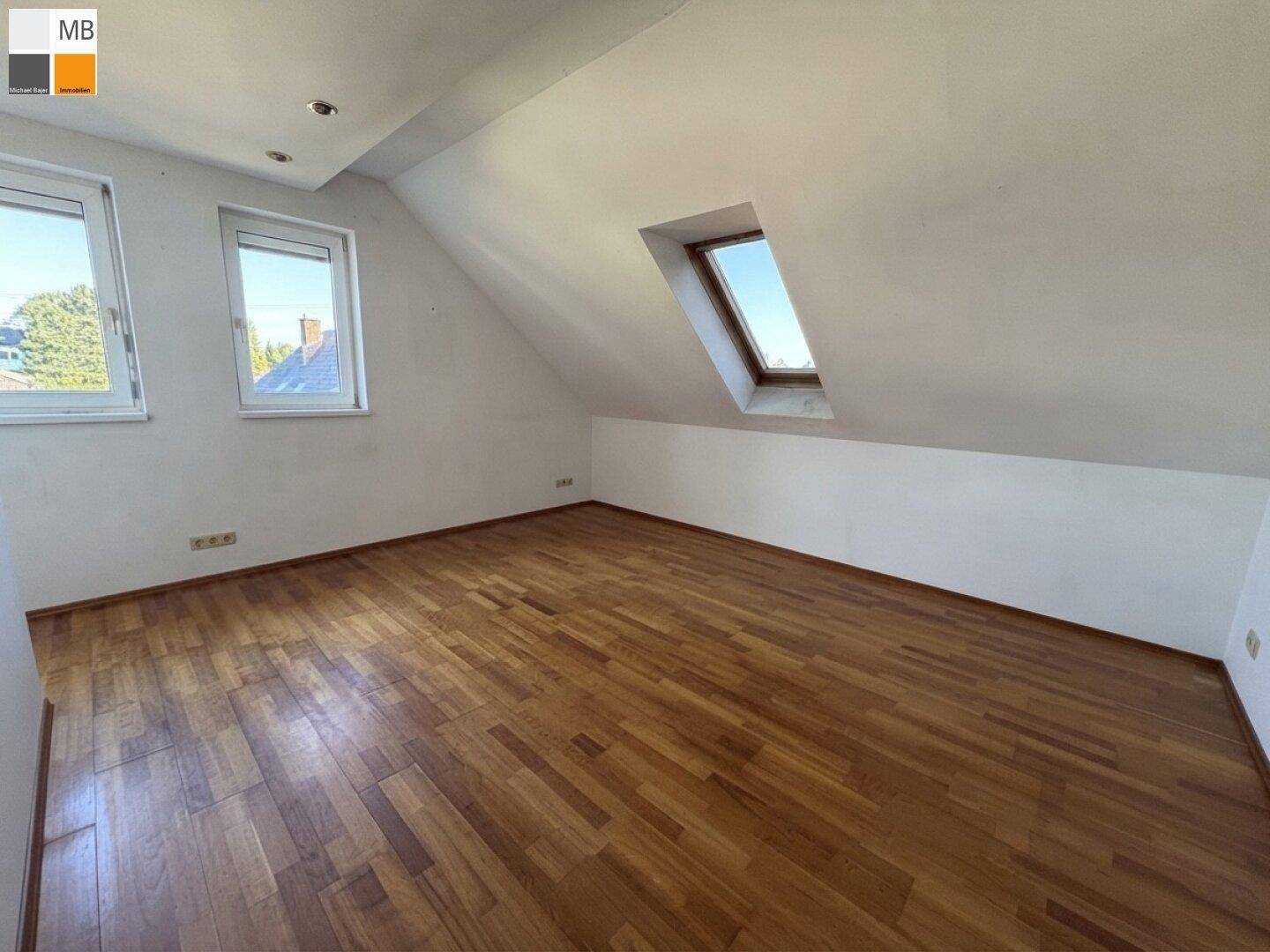 Helles Zimmer mit Holzboden, Dachschrägen und einer Kombination aus normalen und Dachfenstern.