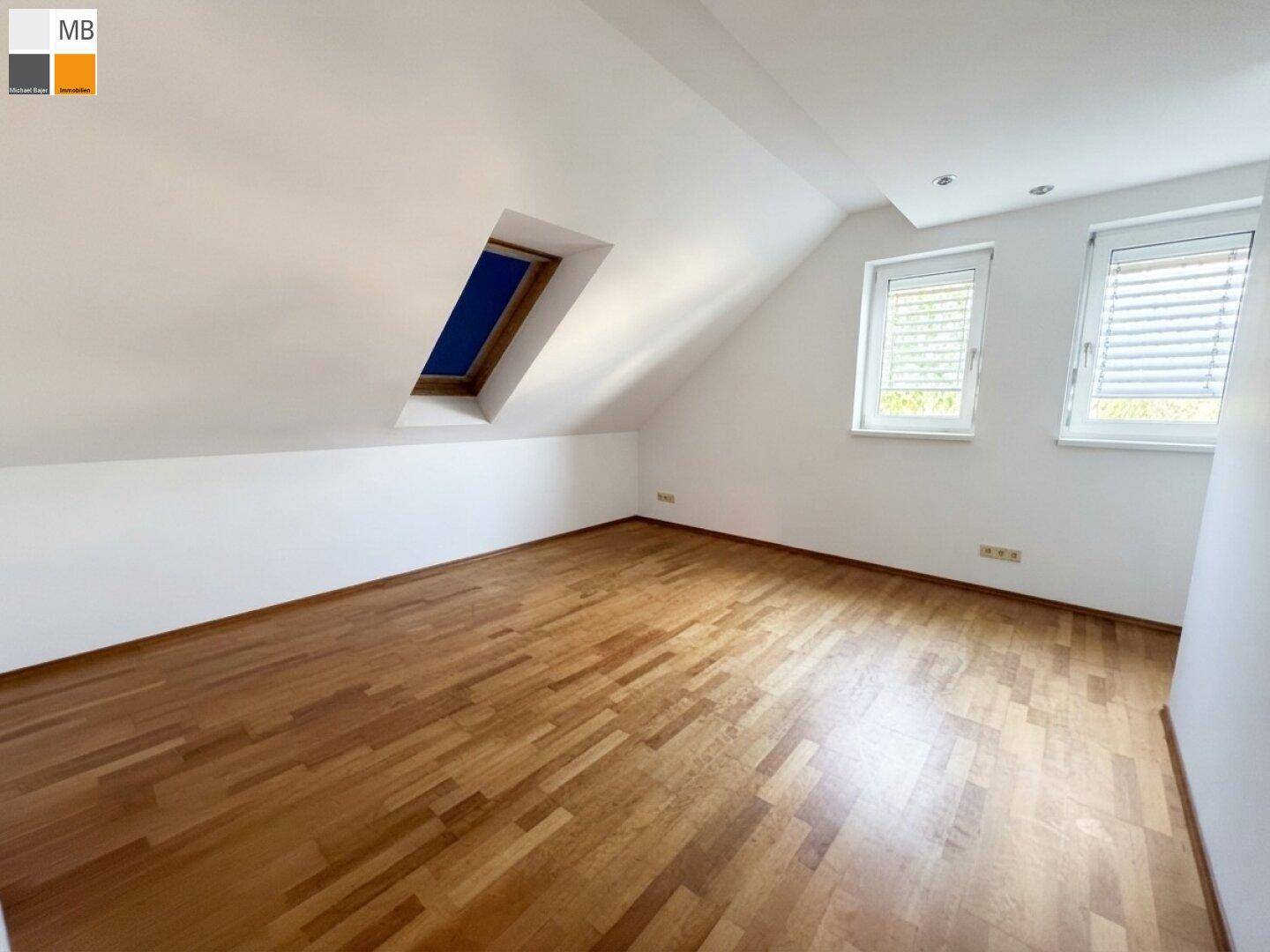 Freundliches Zimmer mit Holzboden, Dachschrägen und viel Tageslicht durch mehrere Fenster.