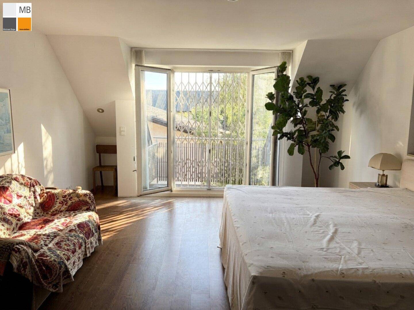 Helles Schlafzimmer mit Holzboden, großem Bett und französischem Balkon mit Blick ins Grüne.