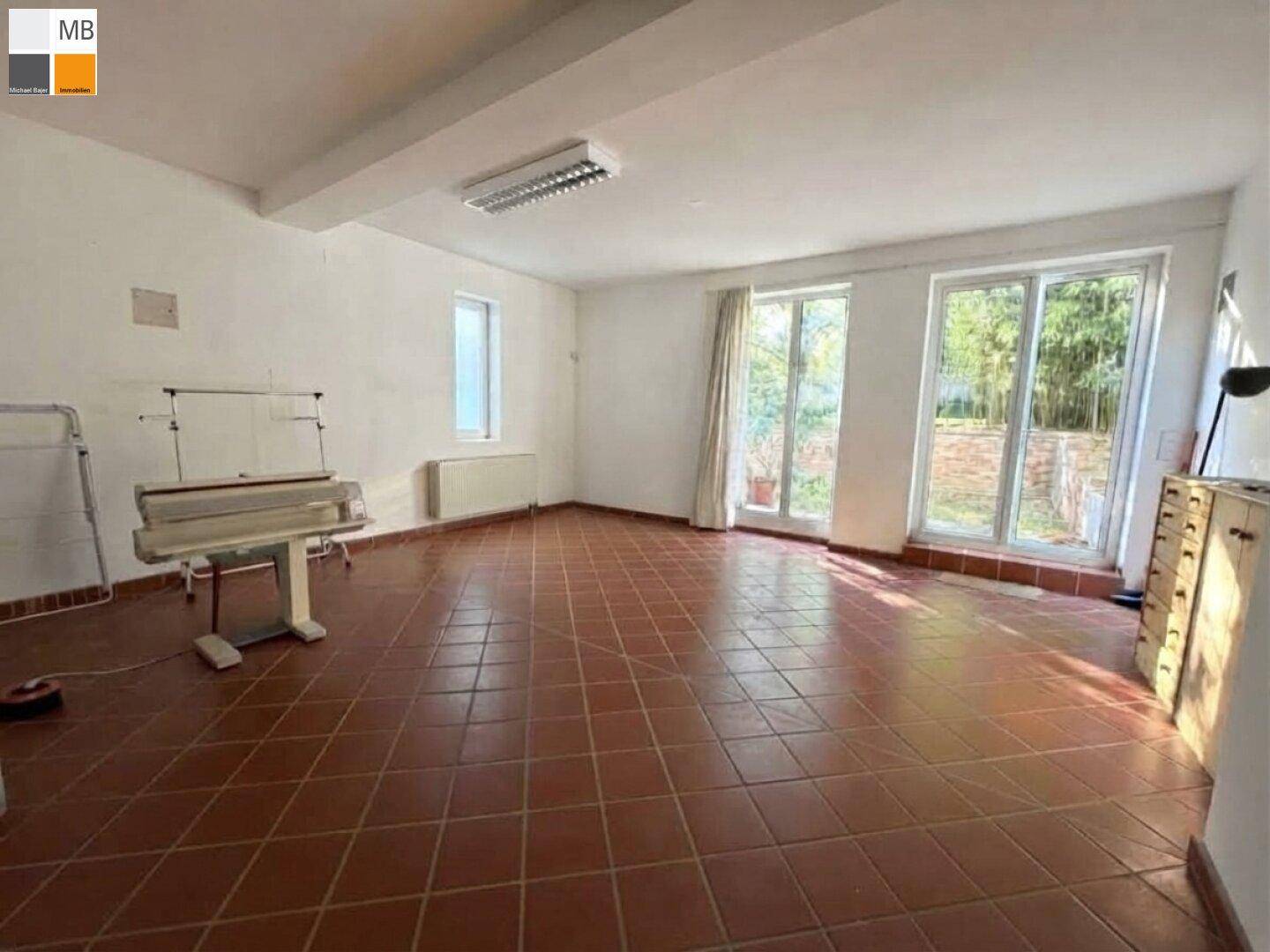 Großer Raum mit Terrakotta-Fliesenboden und großen Fenstern, ideal als Hobby- oder Arbeitszimmer.