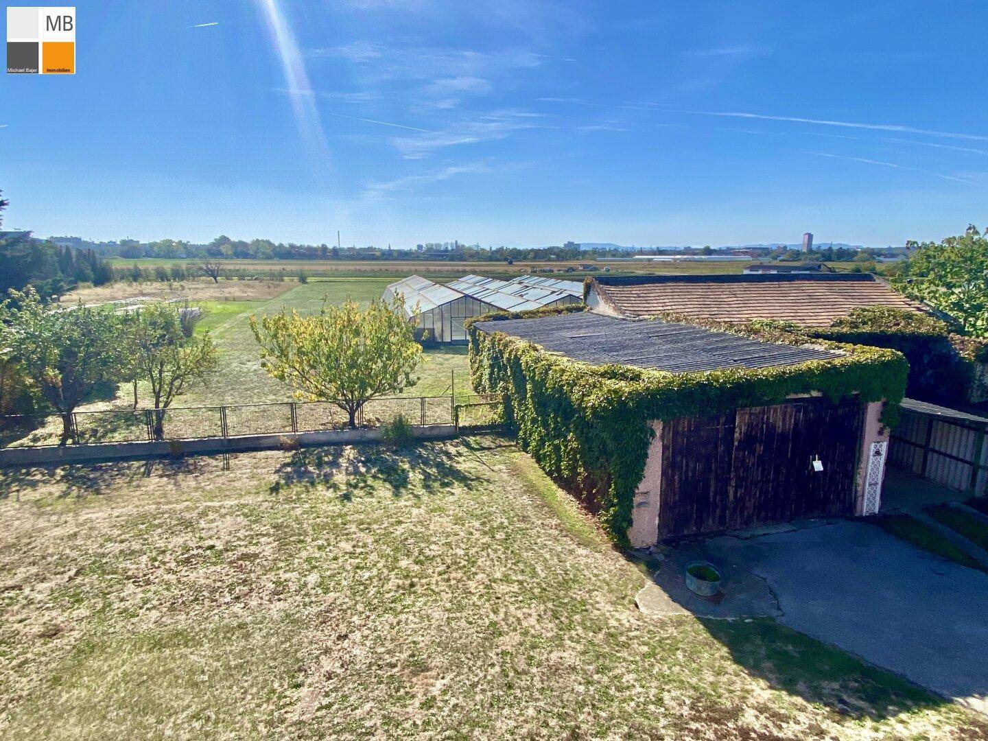 Hinterhof mit Garage, umgeben von Grünflächen und Gewächshäusern in der Ferne.