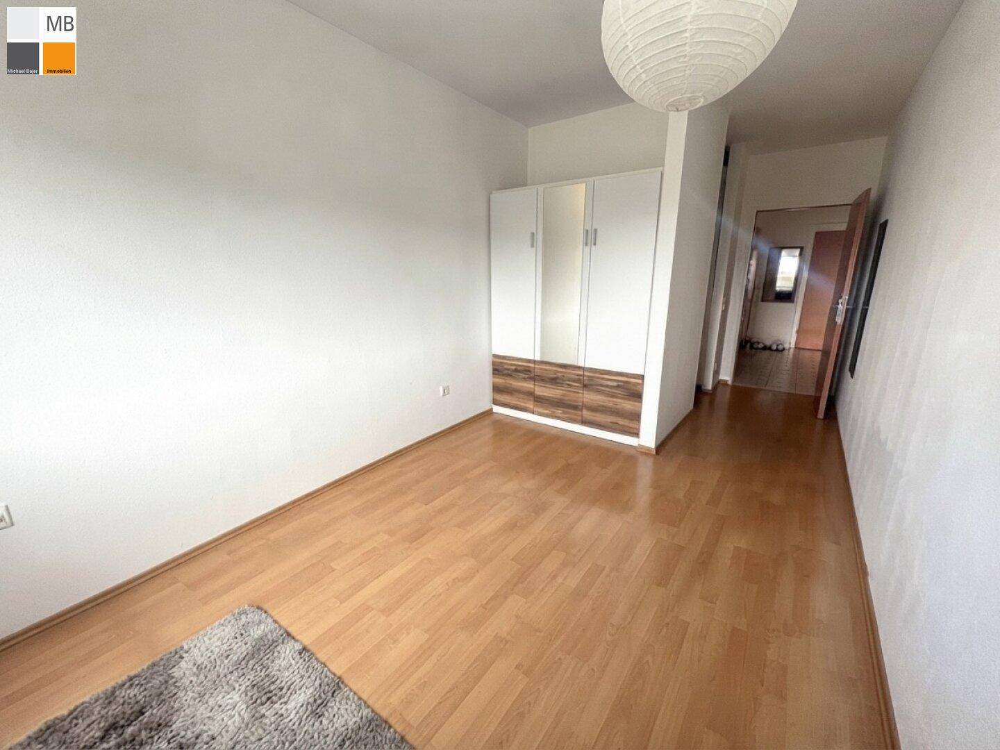 Schlafzimmer mit hellem Parkettboden und integriertem Kleiderschrank, gut beleuchtet.