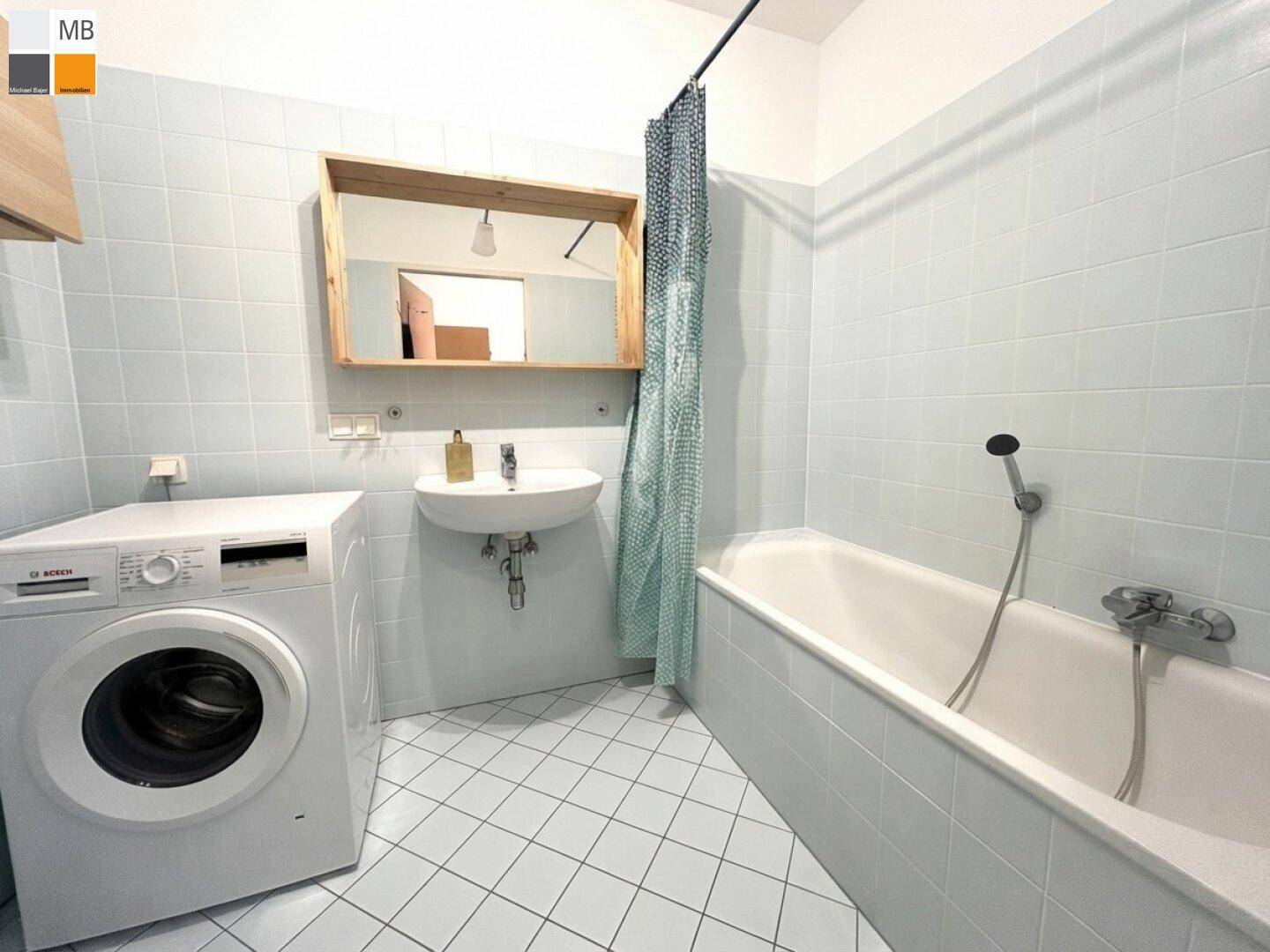 Badezimmer mit Badewanne, Waschmaschine und hellblauen Fliesen an Wänden und Boden.