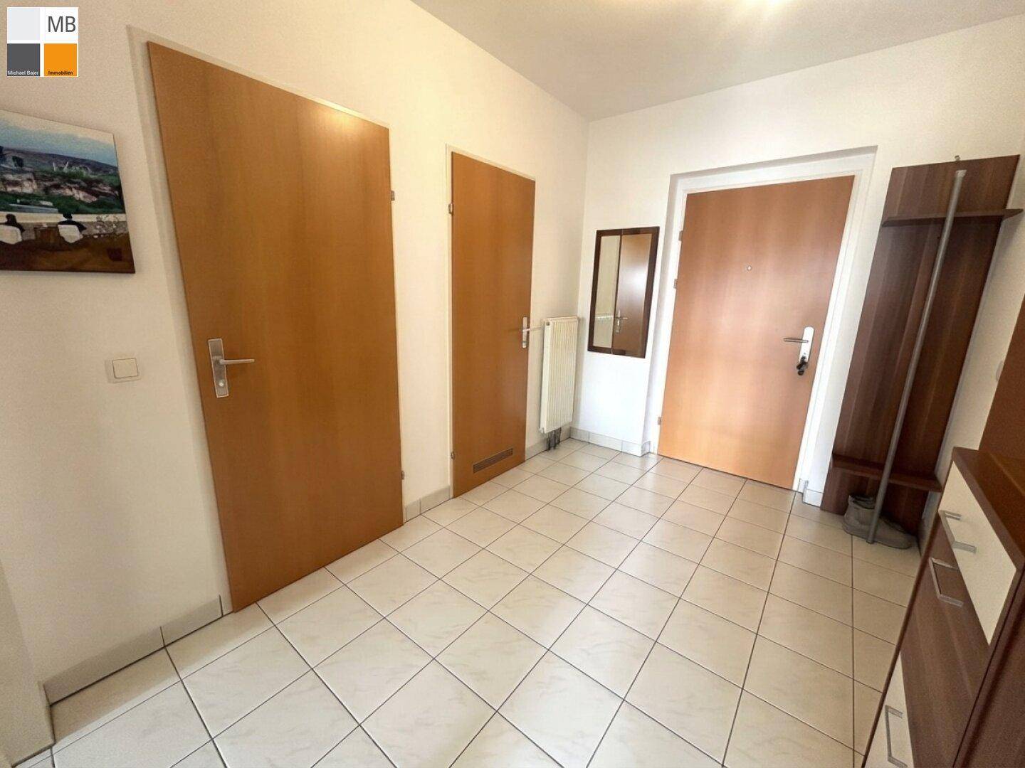 Eingangsbereich mit Fliesenboden, mehreren Türen und Garderobenmöbeln.