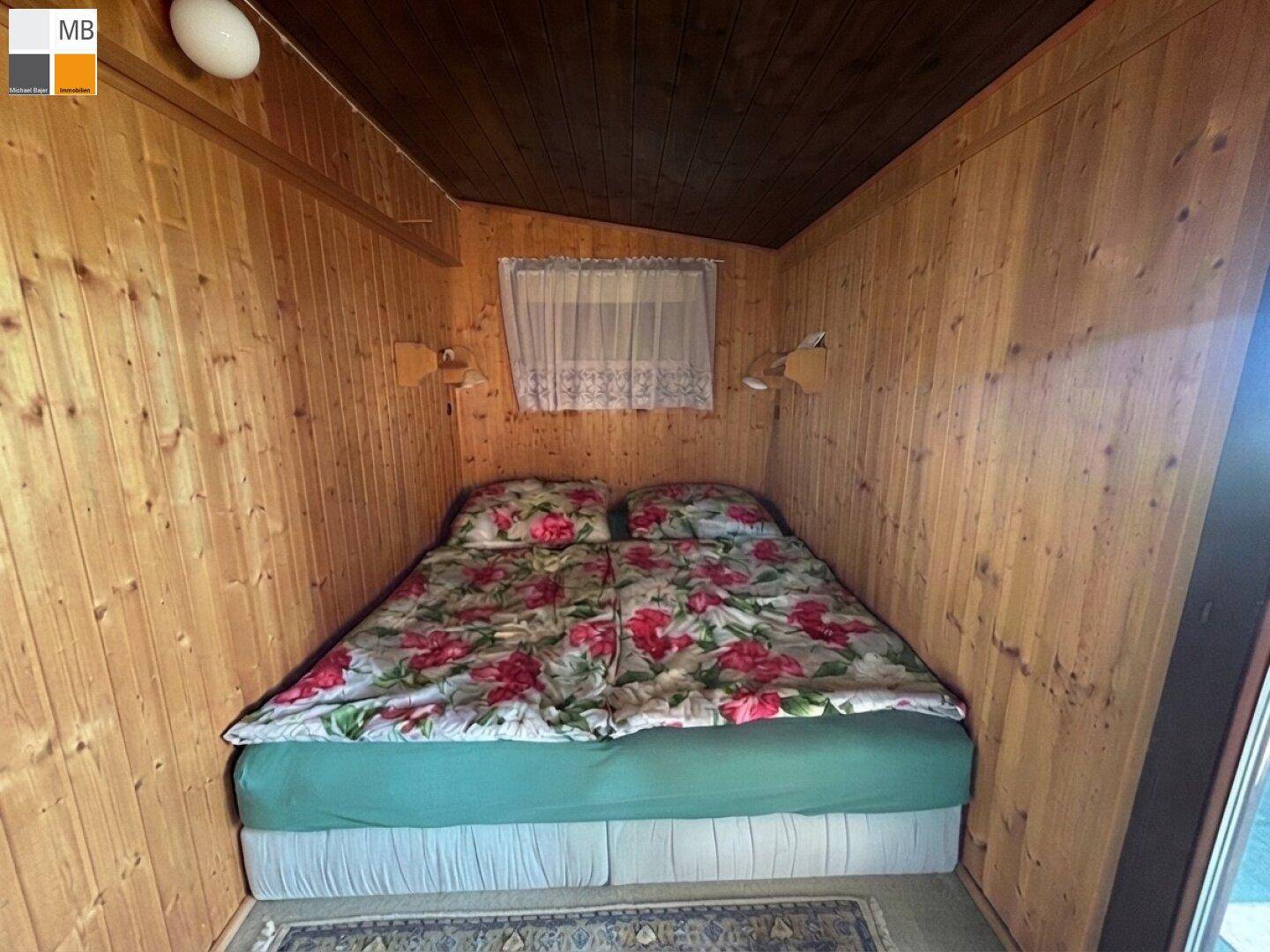 Kleines Schlafzimmer mit Doppelbett, floraler Bettwäsche und Holzvertäfelung.