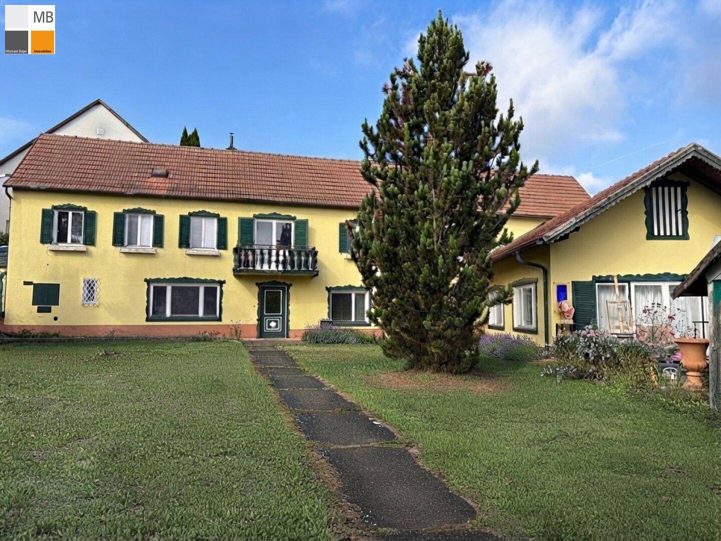 Gesamtansicht des gelben Hauses mit Anbau, Balkon und gepflegtem Rasenbereich im Vordergrund.