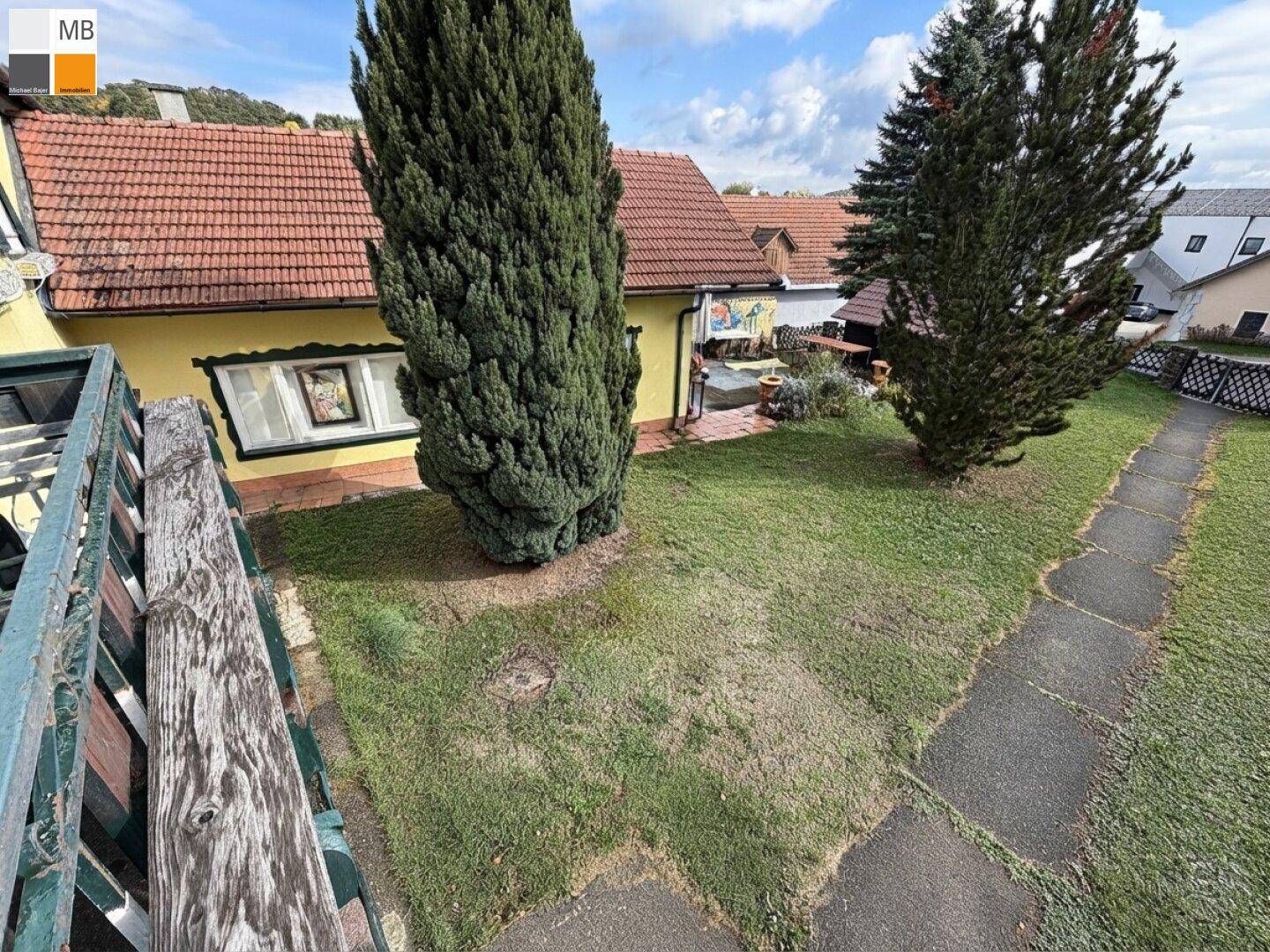 Blick von oben auf den Gartenbereich mit Rasen, Bäumen und einem Teil des Nebengebäudes.
