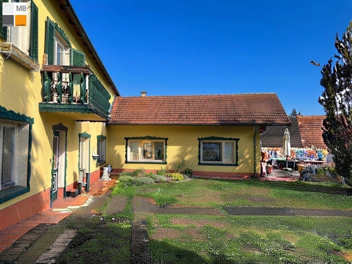Gelbes Haus mit kleiner Terrasse und Gartenmöbeln an der Seite, umgeben von Grün.