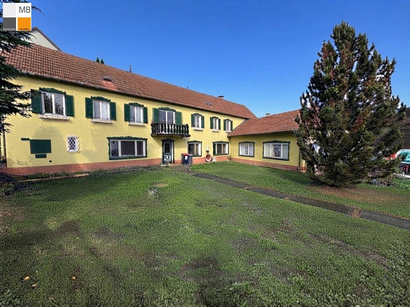 Seitenansicht des gelben Hauses mit traditionellen grünen Fensterläden und rotem Ziegeldach.