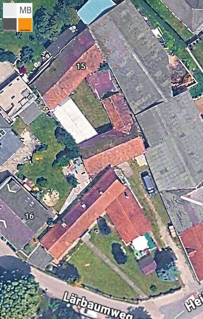 Eine Luftaufnahme, die mehrere Wohnhäuser mit roten Dächern, Gärten und eine Straße in einer Siedlung zeigt.