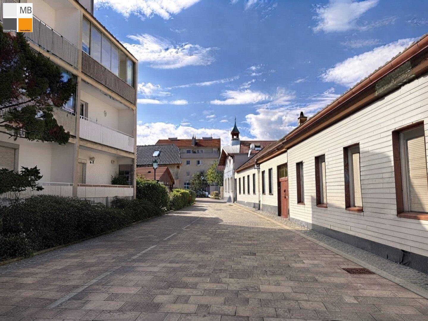 Ruhige Wohnstraße mit modernen und traditionellen Gebäuden unter blauem Himmel und Wolken.