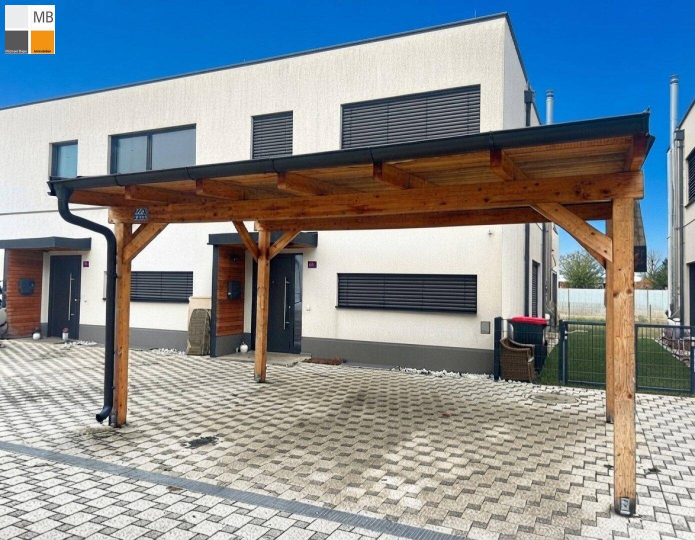 Modernes Gebäude mit einem hölzernen Carport und gepflastertem Vorplatz.