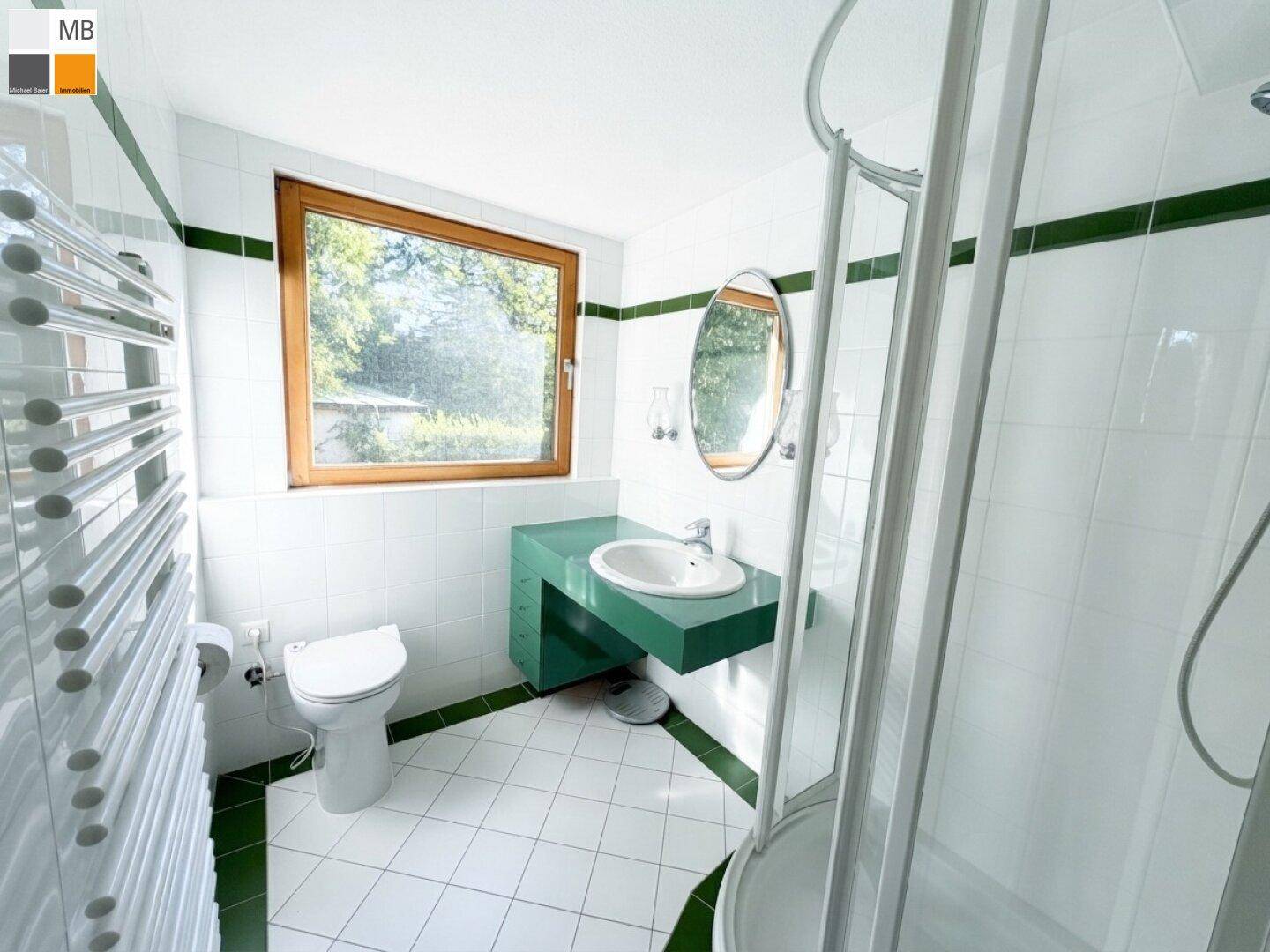 Modernes Badezimmer mit grünen Akzenten, Duschkabine, Waschbecken und beheiztem Handtuchhalter.