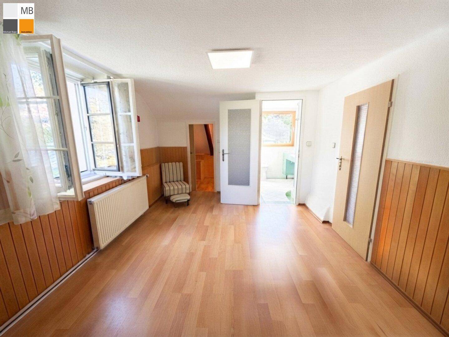 Helles Schlafzimmer mit Laminatboden und Holzvertäfelung, mit Zugang zu einem weiteren Raum.