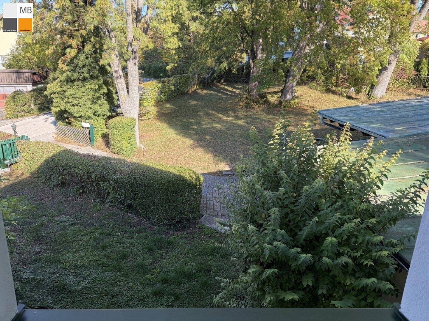 Blick auf den gepflegten Gartenbereich mit Hecken und Bäumen unter blauem Himmel.