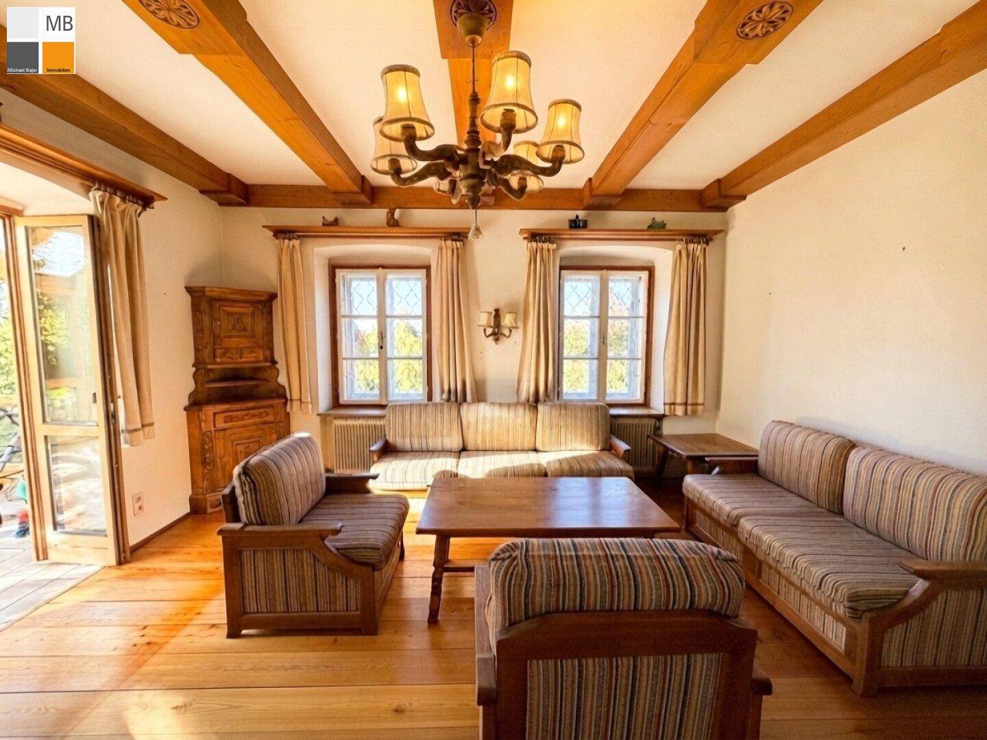 Geräumiges Wohnzimmer mit rustikalen Holzbalken, bequemen Sitzmöbeln und einem Kronleuchter.