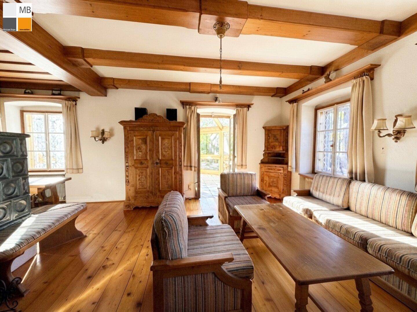 Gemütliches Wohnzimmer im Landhausstil mit Holzbalkendecke, Dielenboden und traditionellem Kachelofen.