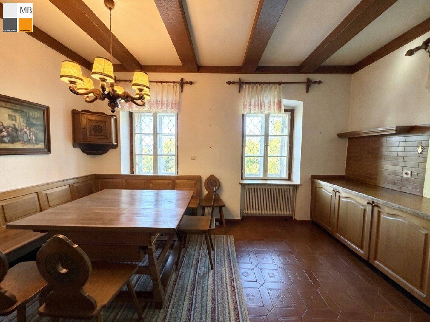 Rustikaler Essbereich mit Holztisch und Eckbank, ergänzt durch eine traditionelle Holzküche im Hintergrund.