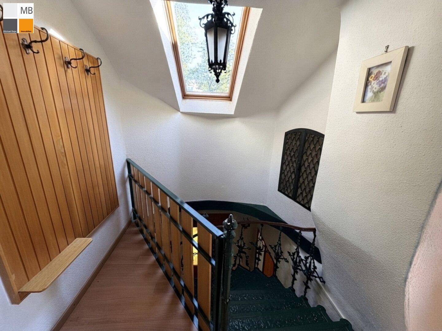 Historisches Treppenhaus mit schmiedeeisernem Geländer und Dachfenster, das Tageslicht spendet.